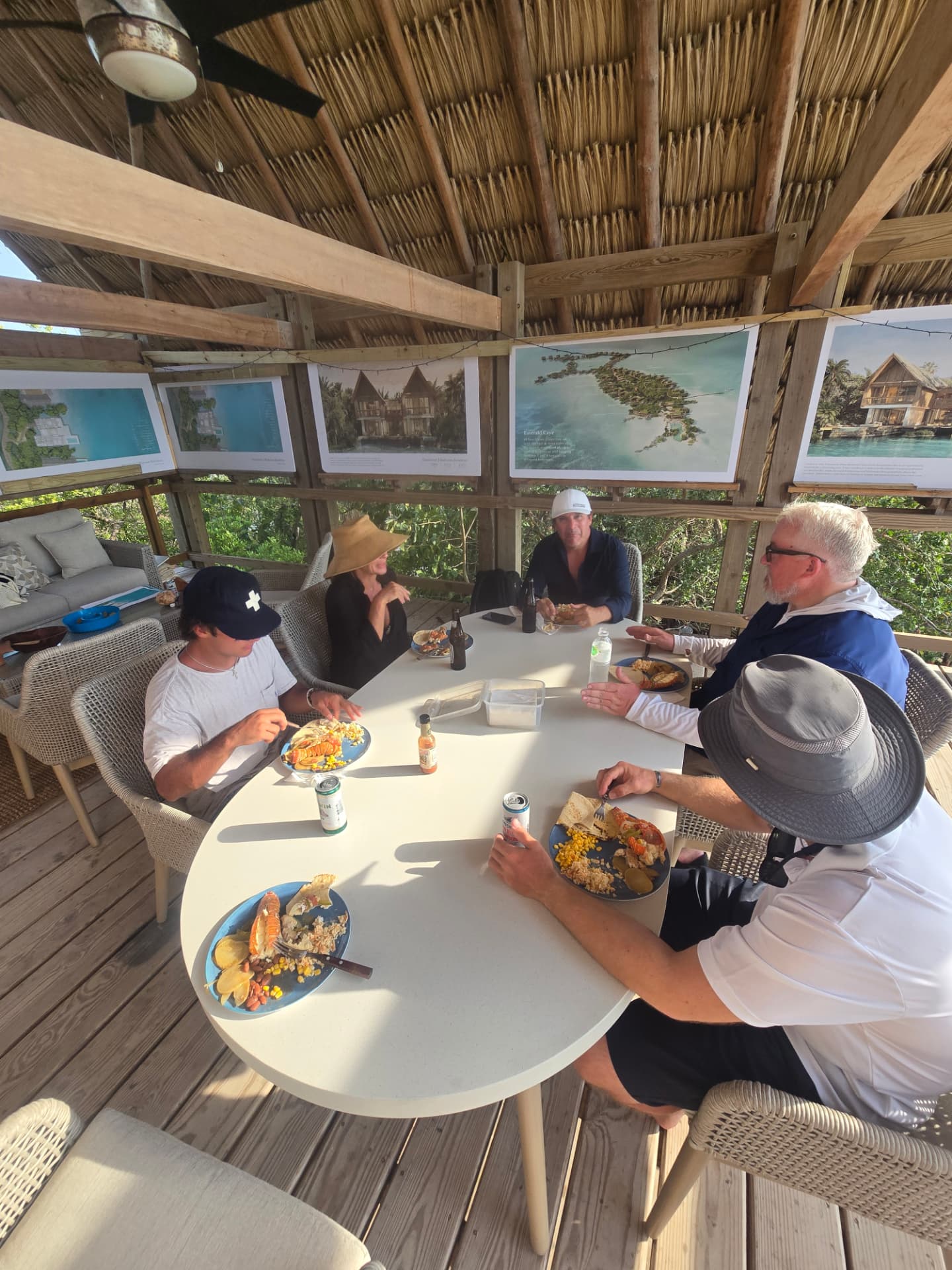 Guests sharing a beach BBQ lunch of their ocean catch under a thatched island pavilion